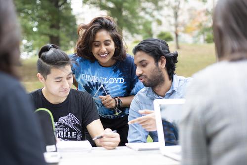Three international students outside studying at a table