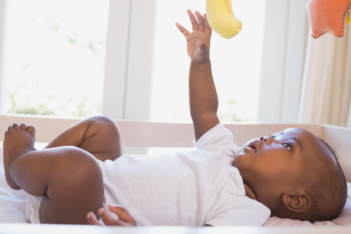 A baby lies in a crib smiling up.