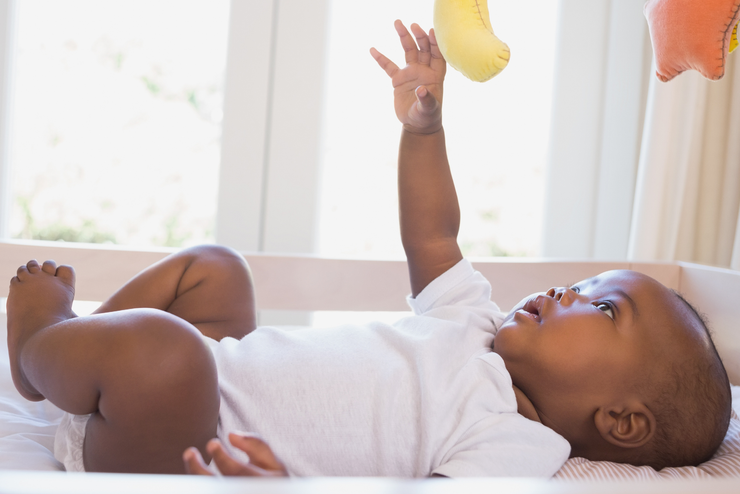 A baby lies in a crib smiling up.