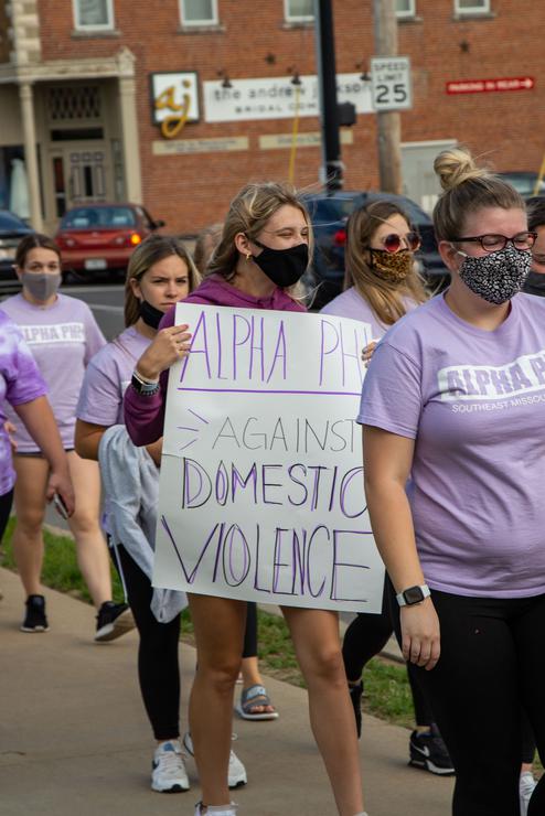 A group of women in purple shirts march with signs about domestic violence.