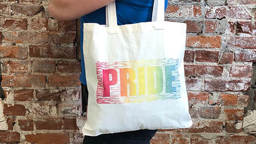 hand printed natural colored canvas bag with the rainbow design that reads 'pride'