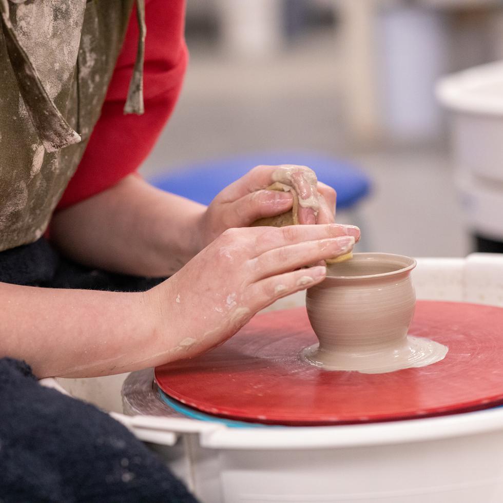 Close-up of two hands creating a pot on a pottery wheel