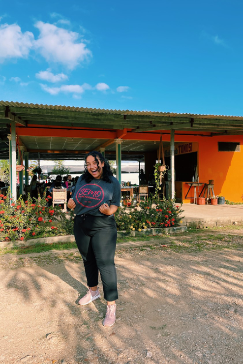 Layla standing in front of an orange building. The covered patio in front of the building is full of people sitting in the shade.