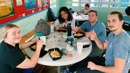 Layla, Nolan, and two others sitting around a table set for lunch. They all smile at the camera.