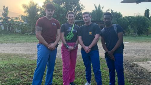 Nolan and three others standing together. They are outside at twilight. 