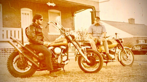Young Torres and a friend sit on motorcycles in front of a house in an old photo.