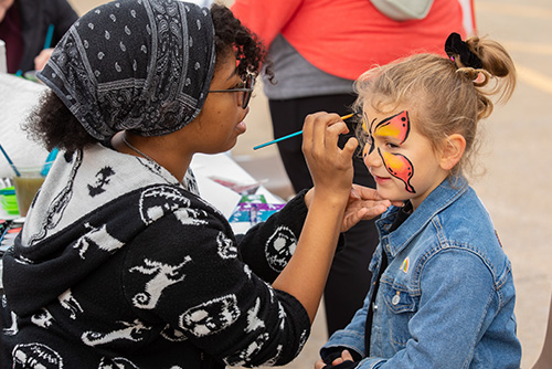 Little girl getting her face painted by a semo student
