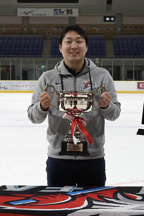 yuhei standing behind a table and proudly holding up an award/trophy