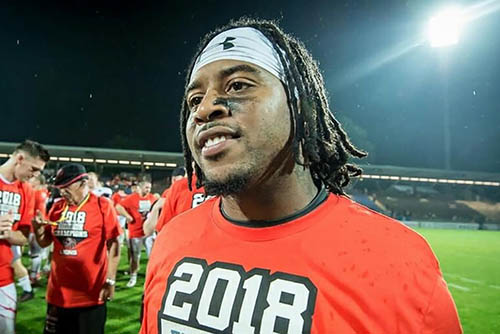 lennies, a young black man, stands on a lit football field wearing a red t-shirt