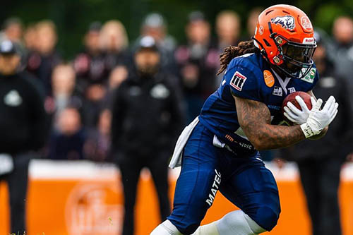 lennies wearing a blue and orange footbal uniform, holding the football to his chest and running