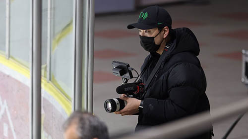 yuhei standing in a hockey stadium wearing a face mask and holding a camera