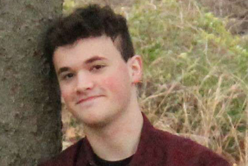 TJ lending up against a tree smiling