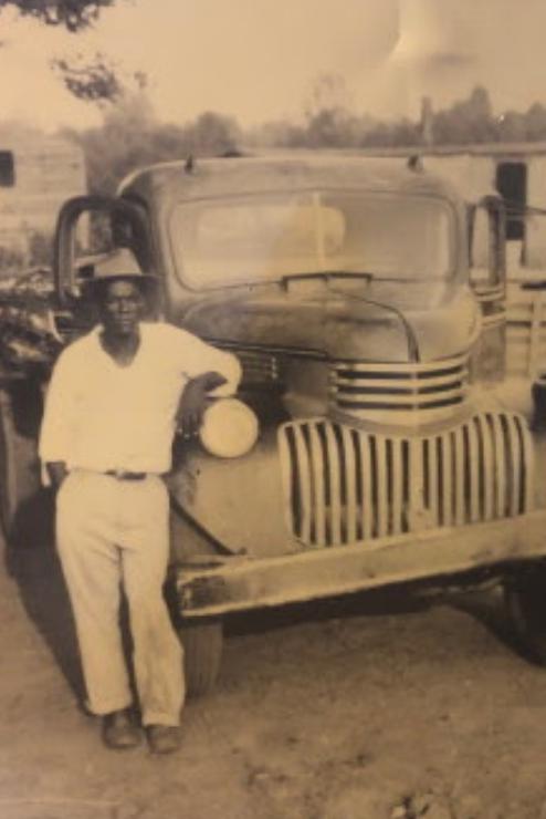 Historic photo of Man standing in front of pick up truck.