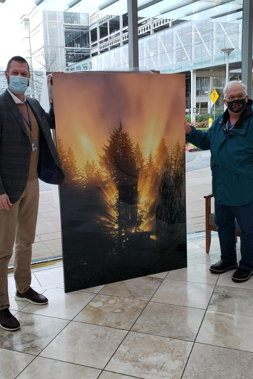 Ron and another man stand next to a large print of one of his landscape photos.