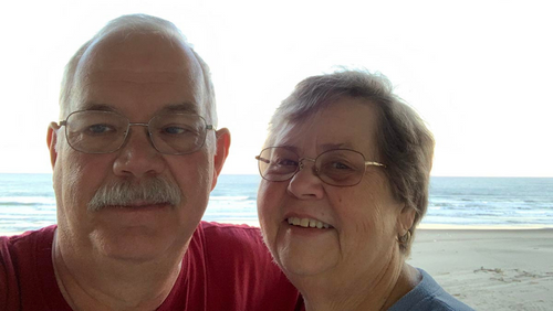 Ron and Jan smile near a beach on vacation.