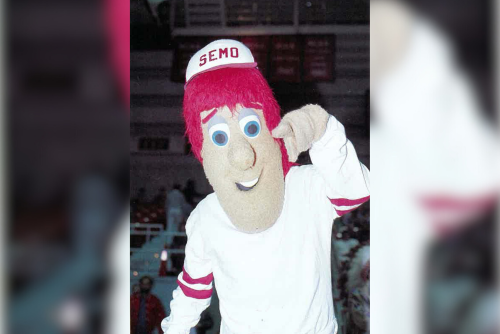 SEMO Red waves to the camera. He is a mascot with a large head and red hair in SEMO attire.