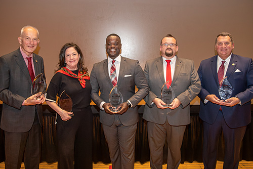 Five people stand together smiling displaying awards