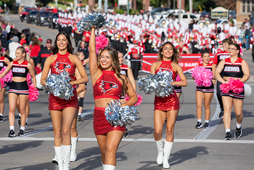 cheerleaders smile and hold pom poms while they walk down the street