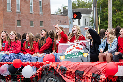 Girls sit on a float and yell with a sign