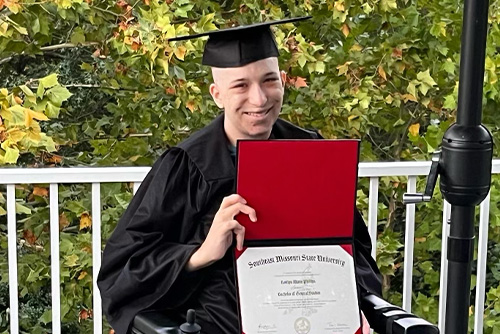 A girl holds up a diploma from Southeast and smiles in a graduation cap