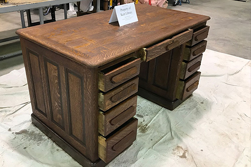 A desk sits in a workspace with a card that says "Property of Kent Library"