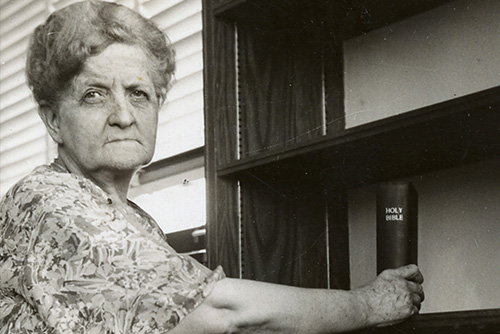 A woman, Sadie Kent, places a Holy Bible on an empty book shelf.