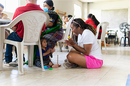 A little girl plays patty cake with a students on the floor