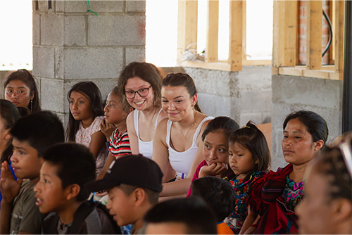 Two students sit among a group of kids
