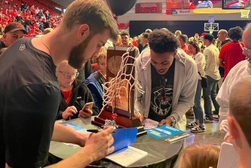 Basketball players sign March Madness tickets for fans.