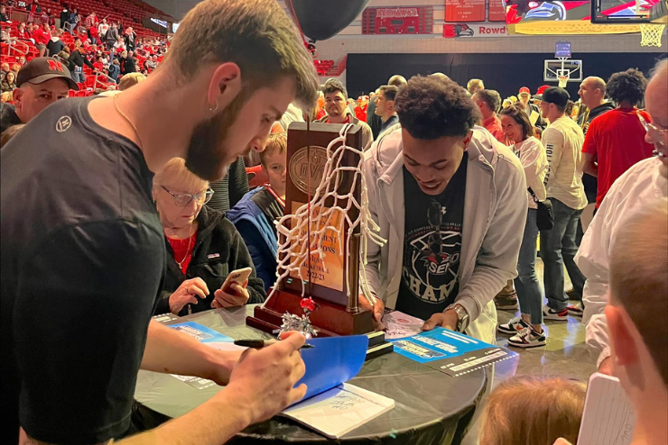 Basketball players sign March Madness tickets for fans.