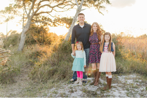 Cdr. Bryce Aubuchon, his wife, and two children smile for a family photo.