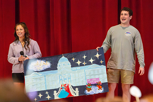 Two greek students holding up a poster that their greek chapters created for Greek Week.