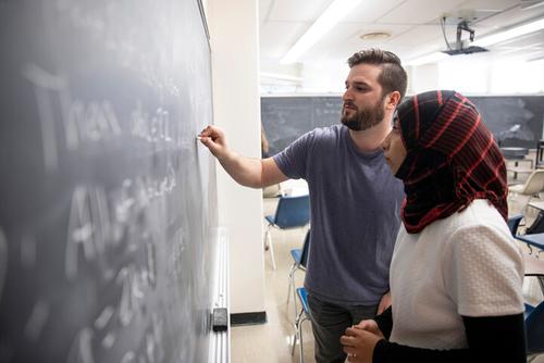 two students standing at a chalkboard working out mathematic formulas