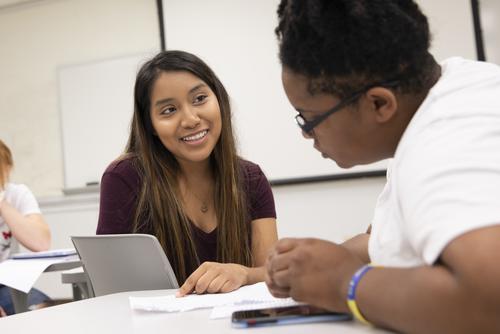 A student smiles while looking at notes with a peer in a Spanish Education class.