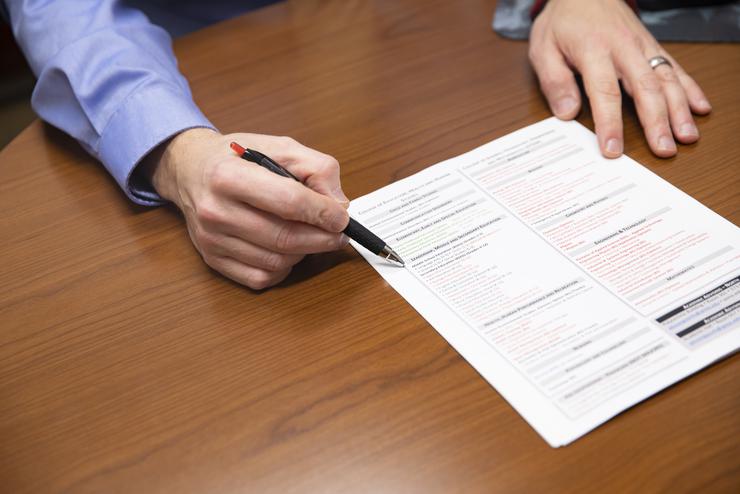 An academic advisor uses a pen to point out sections on a document. 
