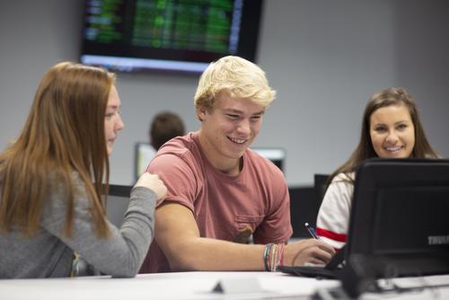 Business students smile while gathered around a computer.