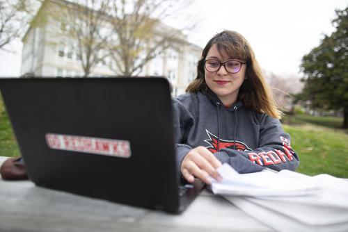 A student in SEMO apparel works on a laptop while sitting at a campus picnic table.