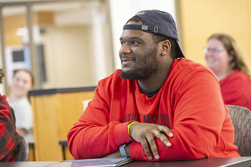 A student works at a laptop while sitting at a classroom desk.