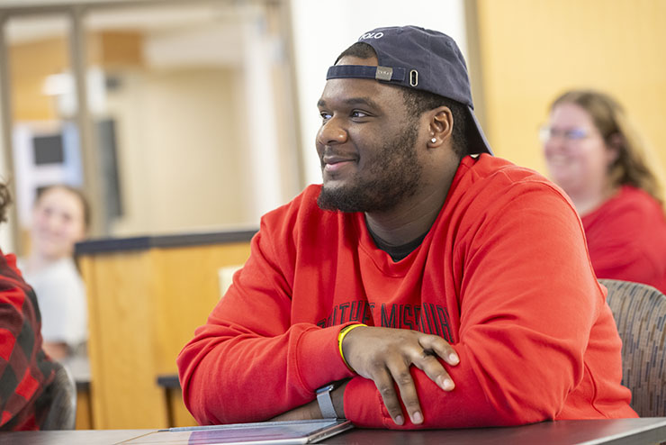 A student works at a laptop while sitting at a classroom desk. 