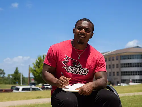 a SEMO student sits outside in the sunshine working on an assignment