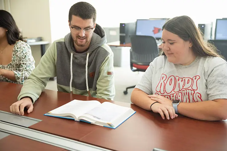 two semo students sit together at a long table and read an assignment