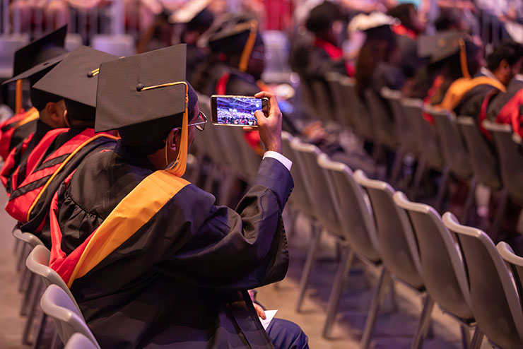 A student points to their diploma while walking across the stage at graduation.