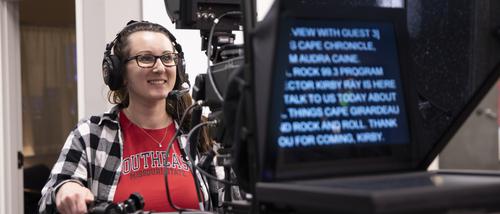 A mass media student smiles while using a teleprompter in a studio.