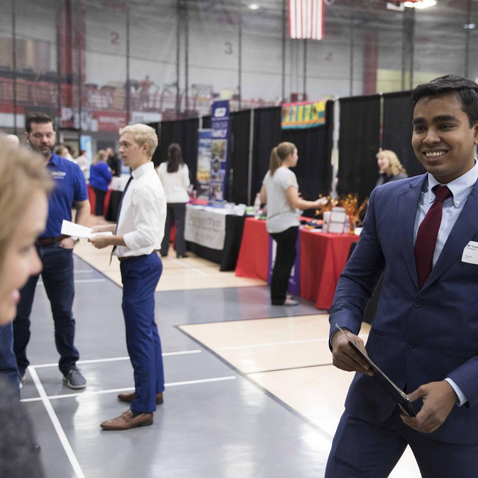 A student in a suit speaks with an industry professional at a career fair.