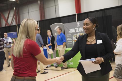 A student shakes hands with an industry professional at a career expo.