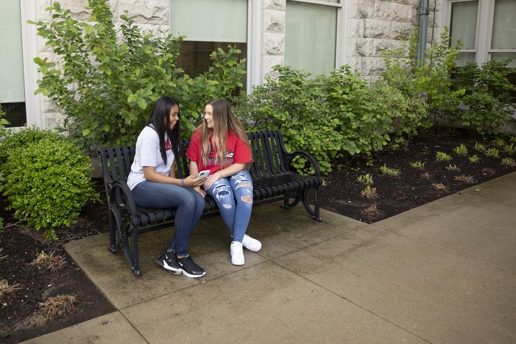 Two students sit on a bench outside Academic Hall. 