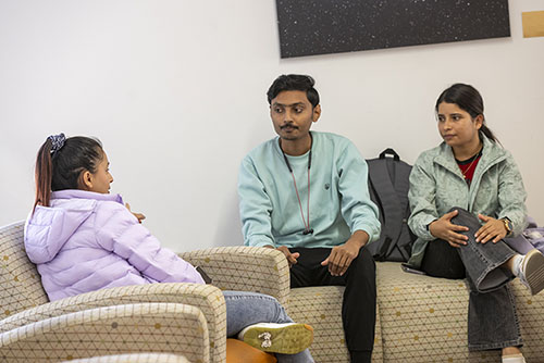 Three students sit on the couches in a student lounge and have a conversation.