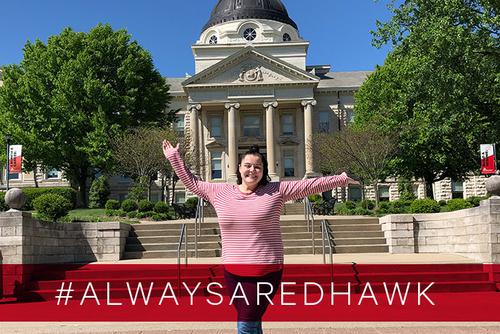 Olivia poses in front of Academic Hall behind the hashtag #alwaysaredhawk.