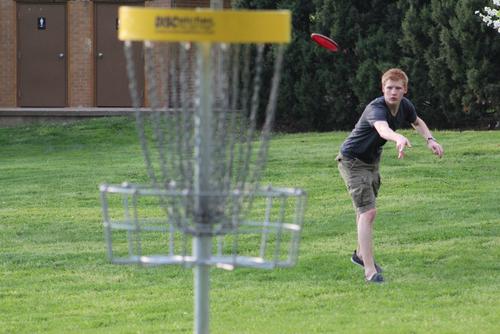 A student throws a disk at a basket at the Capaha Park 10-hole Disc Golf course.