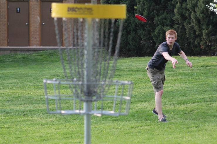 A student throws a disk at a basket at the Capaha Park 10-hole Disc Golf course.